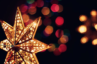 Golden light-up star on dark background with blurred Christmas lights